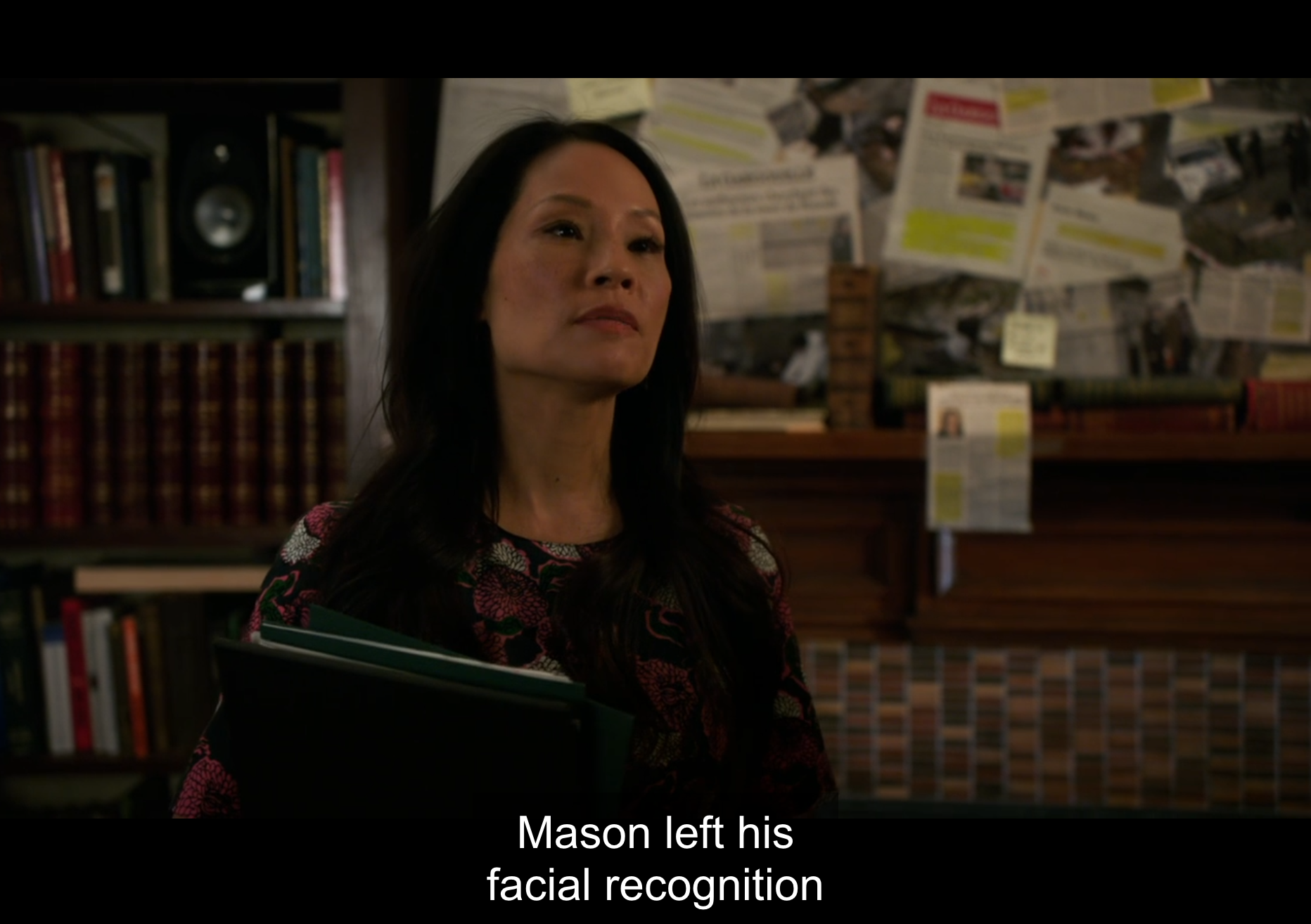 Watson reveals her investigation of Morland Holmes to Sherlock. Se stands in front of a 'murder wall' with articles and photos tacked up and covered in sticky notes. A subtitle reads: "Mason left his facial recognition" (Elementary. 2016a).